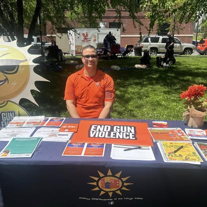PNLV outreach table at a community event with the Mr. Sun banner and END GUN VIOLENCE materials